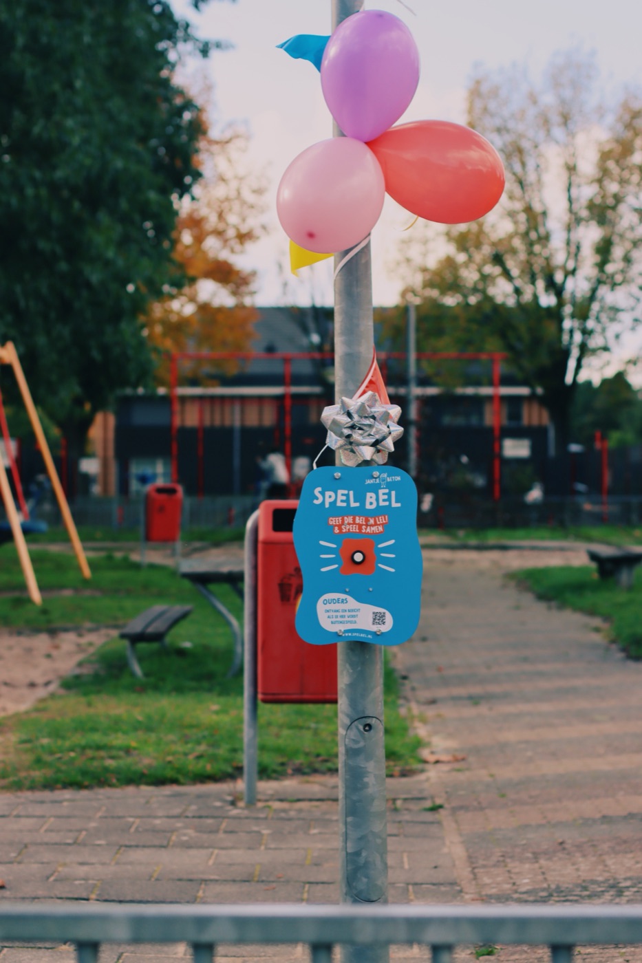 Een SpelBel met het Jantje Beton-ontwerp aan een paal in de speeltuin, versierd met ballonnen